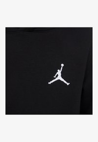 Felpa nera con logo Jumpman ricamato bianco sul lato sinistro del petto. Il materiale sembra morbido, con una trama liscia.