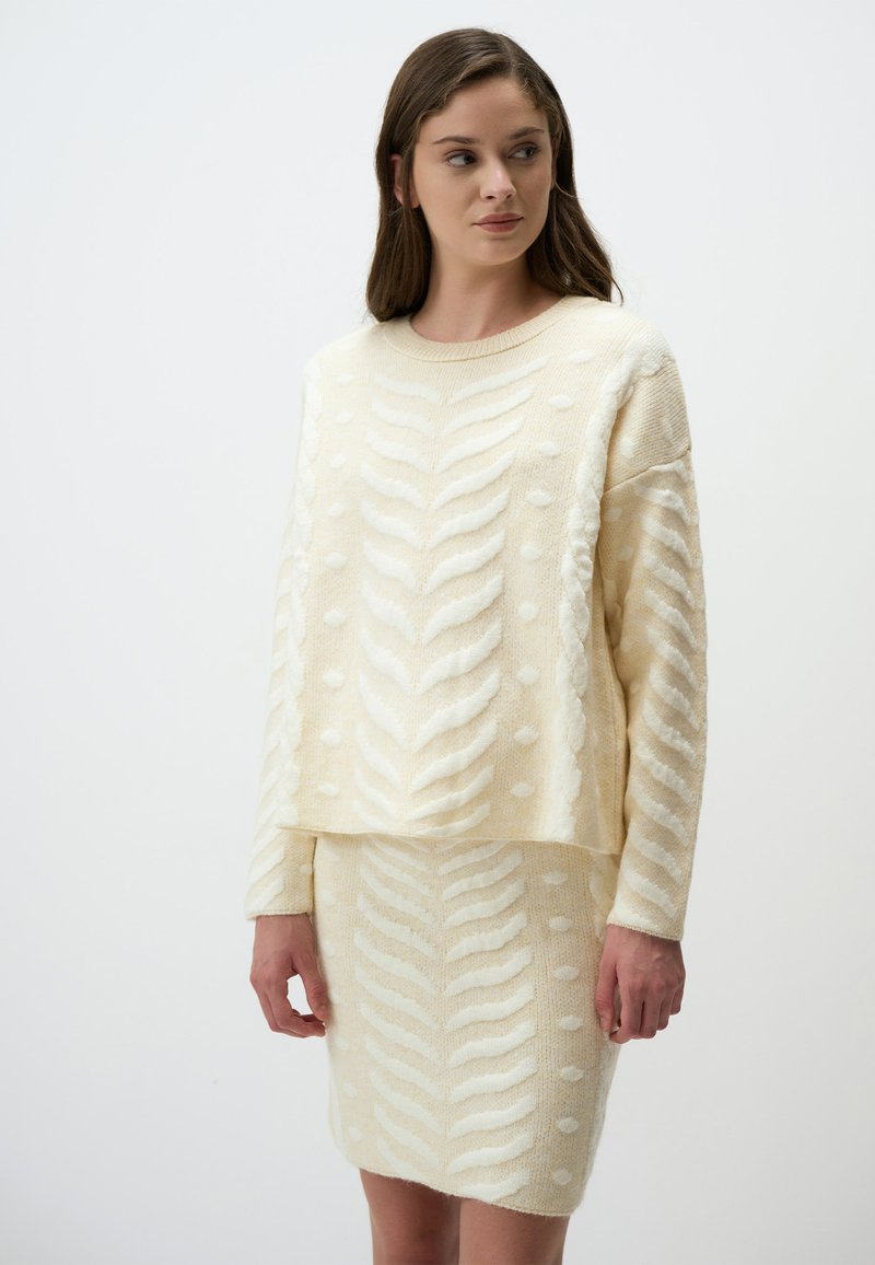 Completo maglione e gonna color crema a maglia con motivi a foglia in rilievo e pois, maniche lunghe e vestibilità rilassata. Tessuto morbido e strutturato.