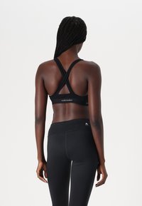 Black sports bra with a cross-back design and soft fabric, paired with high-waisted black leggings featuring a small logo on the waistband.