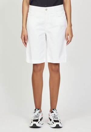 Weiße Baumwoll-Bermudashorts mit lässiger Passform, seitlichen Taschen und umgeschlagenen Säumen, kombiniert mit schwarz-weißen Sportschuhen.