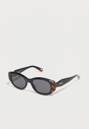 Black cat-eye sunglasses with dark lenses and tortoiseshell accents on the frame edges and temple tips, lying on a white surface.