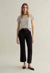 Camicia a righe a maniche corte in crema e nero, abbinata a pantaloni dritti neri a vita alta e ballerine nere a punta.