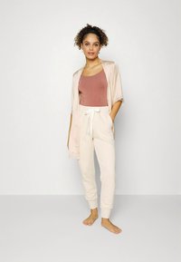 Conjunto de roupa confortável composto por um quimono rosa em cetim, um top justo cor ferrugem e calças de jogging creme claro com cintura ajustável por cordão.