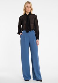 Zwarte doorschijnende blouse met lange mouwen en een strik rond de hals, gecombineerd met op maat gemaakte hoge taille wijde broek in het blauw, met zijzakken.