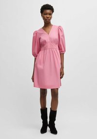 Pink short dress with puff sleeves, V-neck, gathered waistline, and a smooth texture, paired with black knee-high boots.