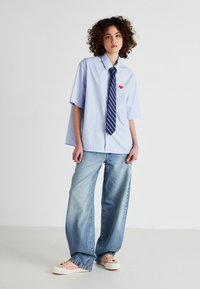 Light blue oversized shirt with short sleeves, red heart appliqué, paired with high-waisted light denim wide-leg pants and pink sneakers.