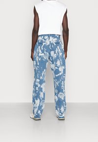 Vaaleansiniset farkut, joissa pilvenkaltaista kulutusta ja abstrakteja kuvioita. Suora lahje ja kaksi takataskua. Yhdistetty valkoiseen yläosaan.