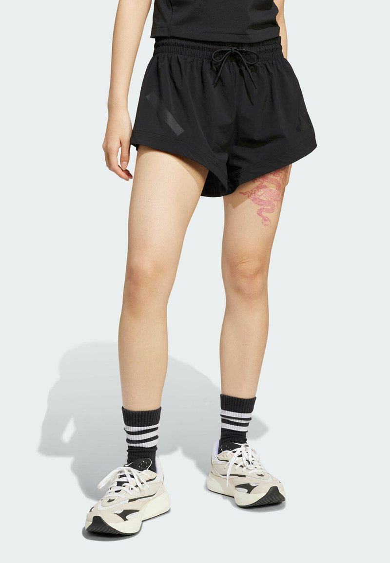 Svarta träningsshorts med elastisk midja och snörning, tillsammans med vita och grå sneakers samt randiga svarta strumpor.