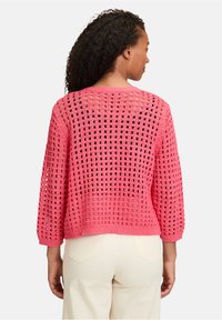 Pull en tricot crochet rose avec un tissage lâche et ouvert, un col rond et des manches trois-quarts. Tissu texturé avec une coupe décontractée.