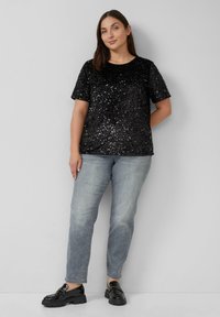 Zwarte pailletten top met korte mouwen en een ronde hals, gecombineerd met lichtblauwe rechte jeans en zwarte patenten instappers.