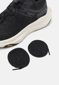 Pantofii de alergare negri au un superior texturat, o talpă intermediară albă cu amortizare și o talpă Vibram, fiind însoțiți de două șireturi negre, rotunde.