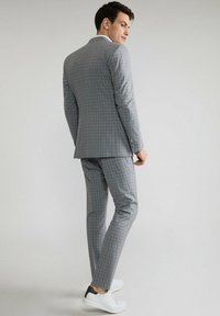 Szary w kratkę garnitur o dopasowanym kroju, z dwu guzikową marynarką i slim fit spodniami. Połączony z białymi trampkami dla luźniejszego akcentu.