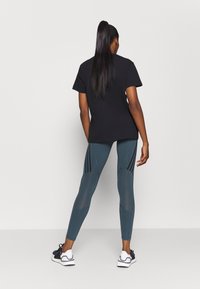 Czarna koszulka, dopasowane turkusowe legginsy z siateczkowymi wstawkami i czarnymi paskami po bokach, w zestawie z czarno-białymi butami sportowymi.