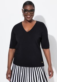 Maglione nero a maniche corte con scollo a V in un tessuto a maglia liscia, abbinato a una gonna a righe verticali bianco e nera. Accento dorato all'orlo.