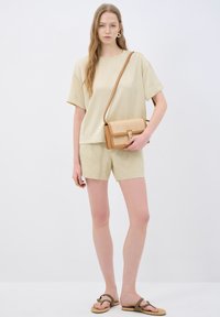 Beige oversized kortærmet top, matchende lyse shorts og en lysebrun crossover-taske med vævet tekstur. Casual fodtøj i brun.