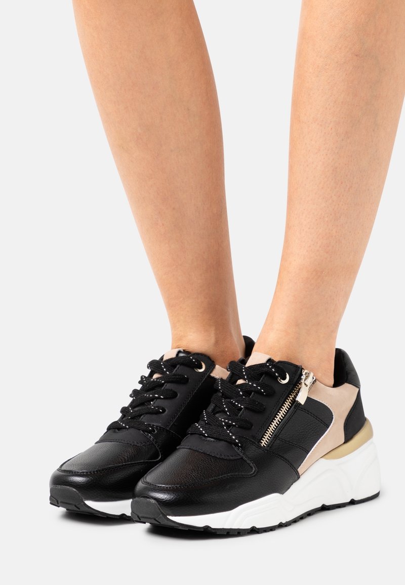 Baskets noires et beiges avec une tige en cuir texturé, lacets à l'avant, détail de fermeture éclair sur le côté, et une semelle plateforme blanche et robuste.