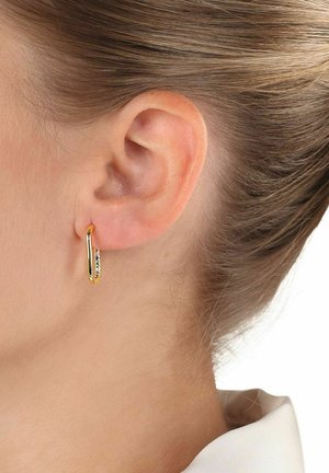 Pendiente de aro dorado con un diseño curvado, que cuenta con pequeñas piedras transparentes a lo largo del borde inferior. Sujetado a la oreja de un modelo en un entorno neutral.