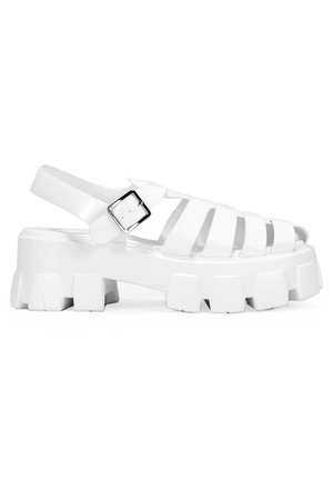 Sandalias de plataforma blancas con múltiples recortes, correa ajustable en el tobillo y suela gruesa con surcos pronunciados y textura suave.