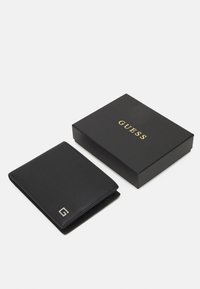 Portafoglio in pelle nera con superficie testurizzata, con logo argentato sul davanti. Viene fornito con una scatola nera che mostra il nome del marchio in oro.