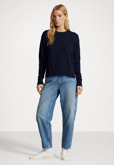 Navy gebreid sweater met ronde hals en geribde zoom, gecombineerd met lichtblauwe hoge taille jeans en witte sneakers.