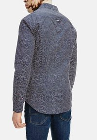 Camicia a maniche lunghe di colore blu scuro con un piccolo motivo floreale multicolore. Presenta un colletto a camicia e un accento con logo sul retro.