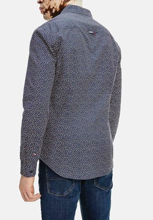 Camicia a maniche lunghe di colore blu scuro con un piccolo motivo floreale multicolore. Presenta un colletto a camicia e un accento con logo sul retro.