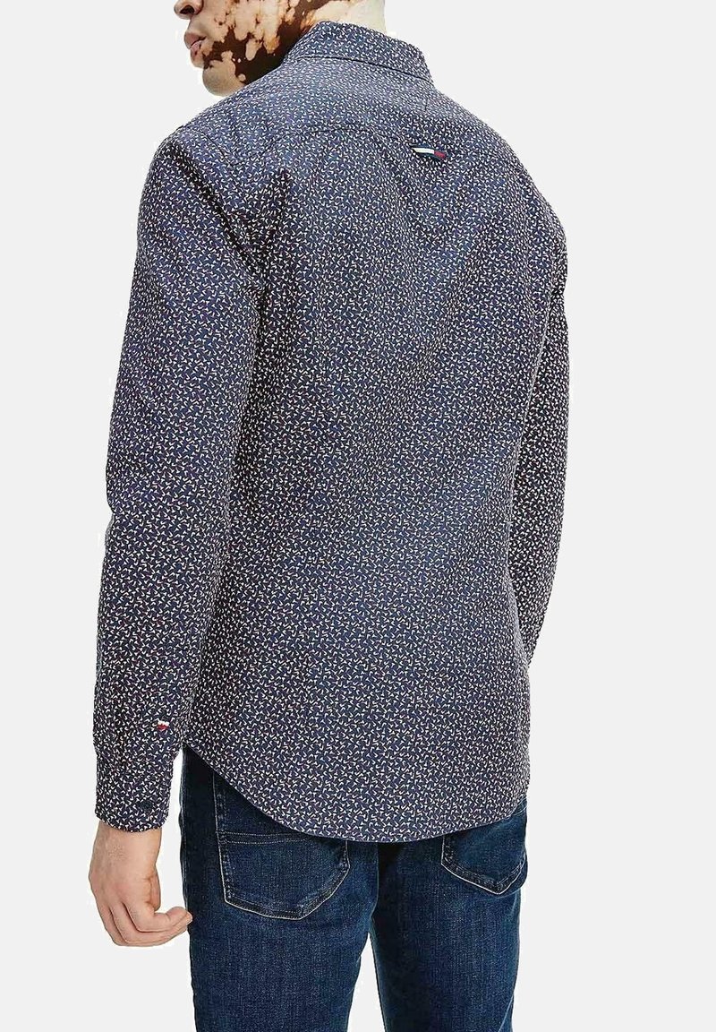 Camicia a maniche lunghe di colore blu scuro con un piccolo motivo floreale multicolore. Presenta un colletto a camicia e un accento con logo sul retro.