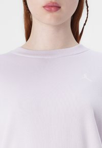 Gaiši purpura, teksturēta auduma crewneck džemperis ar mazu baltu Jordan logotipu kreisajā pusē.
