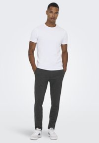 Camiseta blanca de manga corta combinada con pantalones oscuros de rayas grises y zapatillas blancas. Se puede ver la textura rayada en los pantalones.