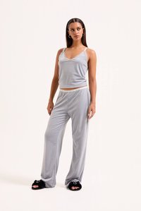 Gaiši pelēks pidžamas komplekts ar mežģīņu apdari krekliņā un brīvi pieguļošas bikses. Audums izskatās mīksts un gluds. Melnas pūkainas čības.