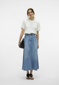 Lichtgewicht crème t-shirt met grafische tekst "COFFEE SKATER", gecombineerd met een lange blauwe denim rok en een zwarte handtas. Zwarte platte sandalen maken de outfit compleet.