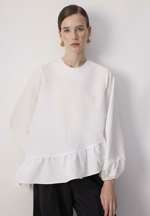 Blusa bianca a maniche lunghe con orlo arricciato, realizzata in tessuto texturizzato. Scollatura rotonda e maniche voluminose creano una silhouette rilassata.