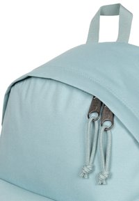 Mochila azul claro hecha de tela texturizada. Presenta una tapa con cierre de cremallera y una asa superior en bucle para un fácil transporte.