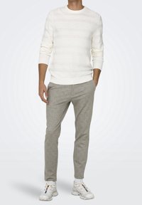 Light beige knit sweater with horizontal stripes, paired with light gray textured trousers and white sneakers. Simple, casual outfit.