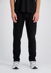Sorte sweatpants lavet af blødt stof med en tætsiddende pasform. Har et tekstureret "ALPHA INDUSTRIES" logo ned ad venstre ben.