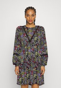 Vestido floral com um fundo escuro e padrões coloridos, mangas longas e decote em V acentuado com detalhes em renda.