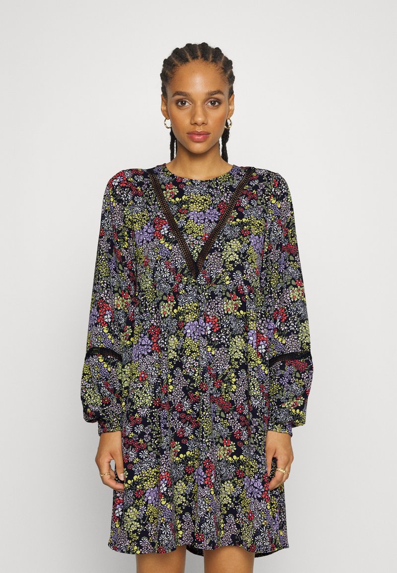 Vestido floral com um fundo escuro e padrões coloridos, mangas longas e decote em V acentuado com detalhes em renda.