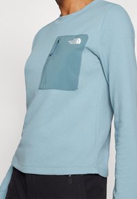 Chemise à manches longues bleu clair avec un motif texturé, dotée d'une poche poitrine zippée et d'un col rond.