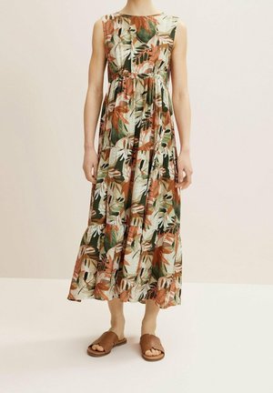 Robe maxi avec un imprimé de feuilles tropicales en vert, orange et crème, dotée d'un corsage ajusté et d'une jupe à volants fluide. Associée à des sandales à glisser marron.