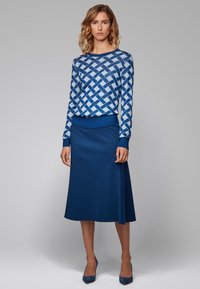Blåmönstrad långärmad topp med ett vävt mönster; kombineras med en enfärgad blå A-linjeformad kjol. Båda plaggen ser ut att vara släta.