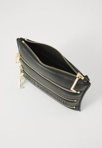 Black clutch bag with gold-tone zippers and hardware. Features embossed branding and a smooth texture with a structured, elongated shape.