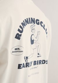 Witte katoenen T-shirt met een grafische print van een hardlopend figuur. De tekst bevat "RUNNING CLUB" en "EARLY BIRDS" in donkerblauw.