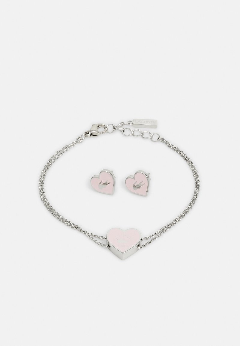 Pulseira de prata em forma de coração com um centro em esmalte rosa e brincos em forma de coração correspondentes. Ambos apresentam um pequeno detalhe de logotipo.