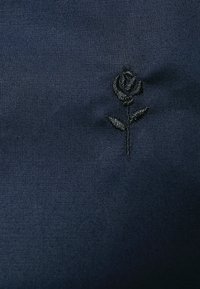 Navy fabric featuring a black embroidered rose with leaves, displaying fine detail in texture and design against a smooth background.