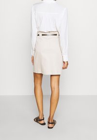 Jupe beige à coupe droite, en tissu lisse. Associée à une chemise blanche à manches longues et des sandales noires à lanières.