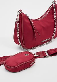 Rød nylon håndtaske med sølvhardware, kædestrop og en glat tekstur. Inkluderer en matchende lille lynlåspose og en aftagelig skulderrem.