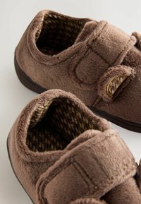 Chaussures marron à texture douce, avec une sangle Velcro, de forme arrondie et un intérieur à motif. Semelle légèrement surélevée.