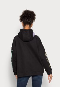 Zwarte oversized hoodie met een kap aan de achterkant, voorzien van grafische accenten in paars en lichtblauw op de mouwen en een gladde, zachte textuur.