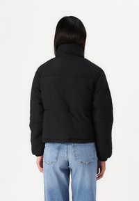 Svart cropped pufferjakke med høy krage, laget av et glatt, teksturert stoff. Belagt overflate uten synlig maskinvare eller mønstre.