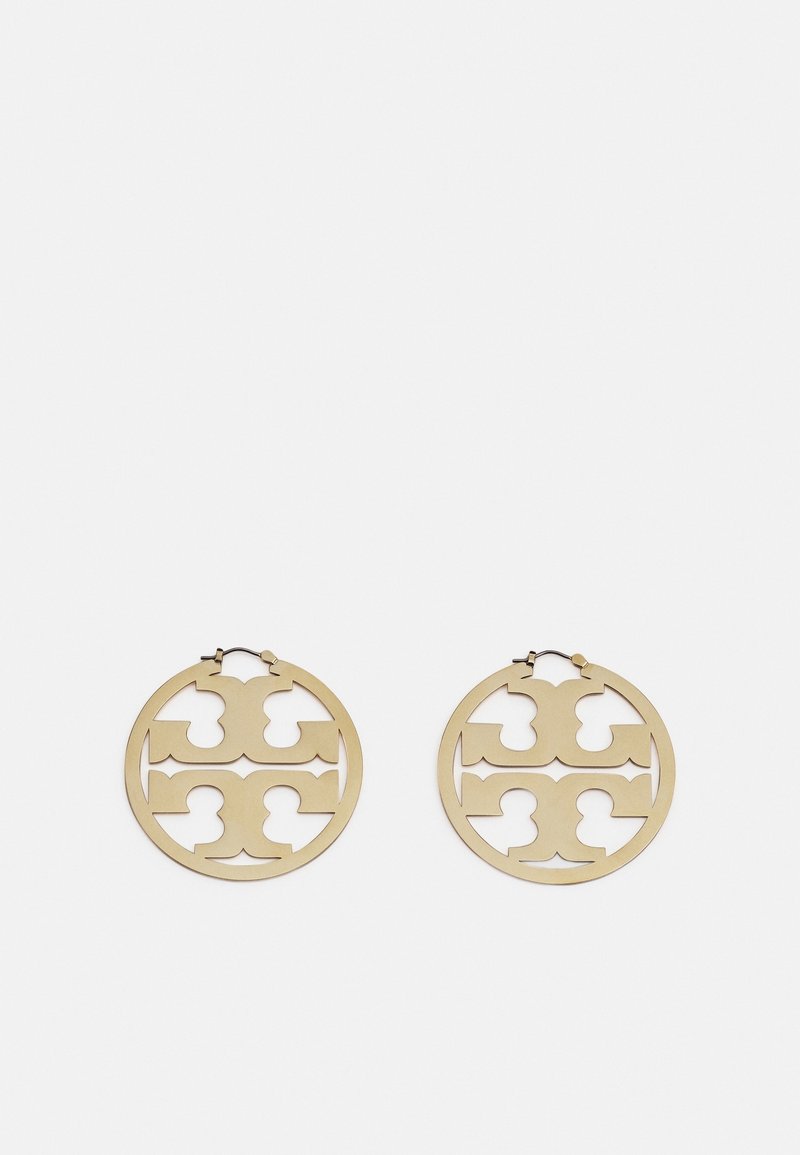 Boucles d'oreilles créoles rondes ton or avec motifs découpés symétriques et fermoirs à charnière sur un fond clair uni.